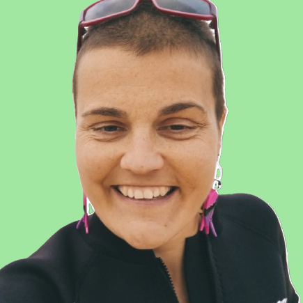 Angélica Gómez Anciana sonriente con gafas y cabello rosa sobre fondo verde.