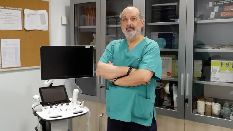 Dr. Calviño de pie en un consultorio con equipo médico y muebles en el fondo.